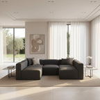 Modern living room with a large gray sectional sofa, abstract painting, and large windows.